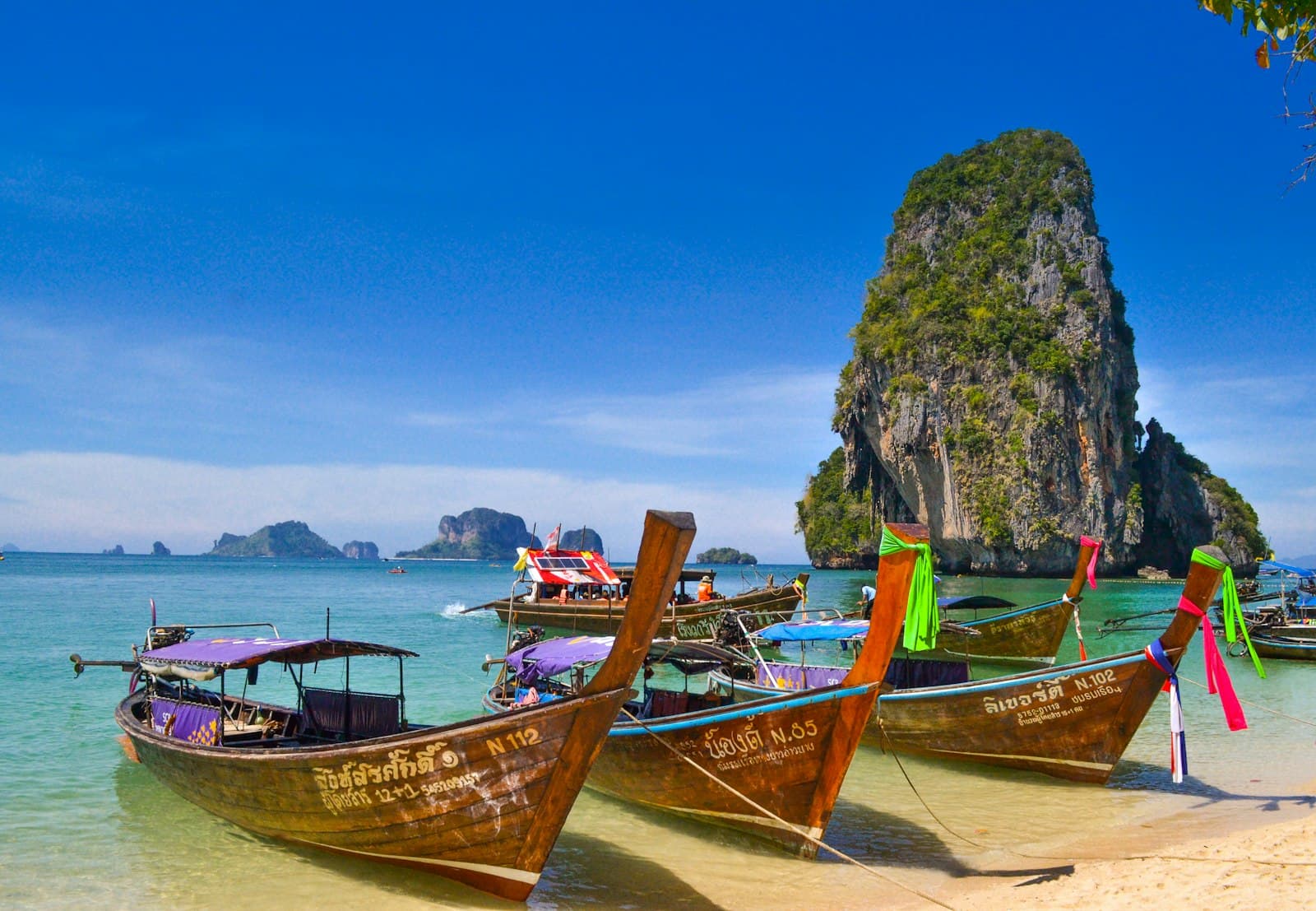 Longtail boats moored beneath a towering limestone cliff